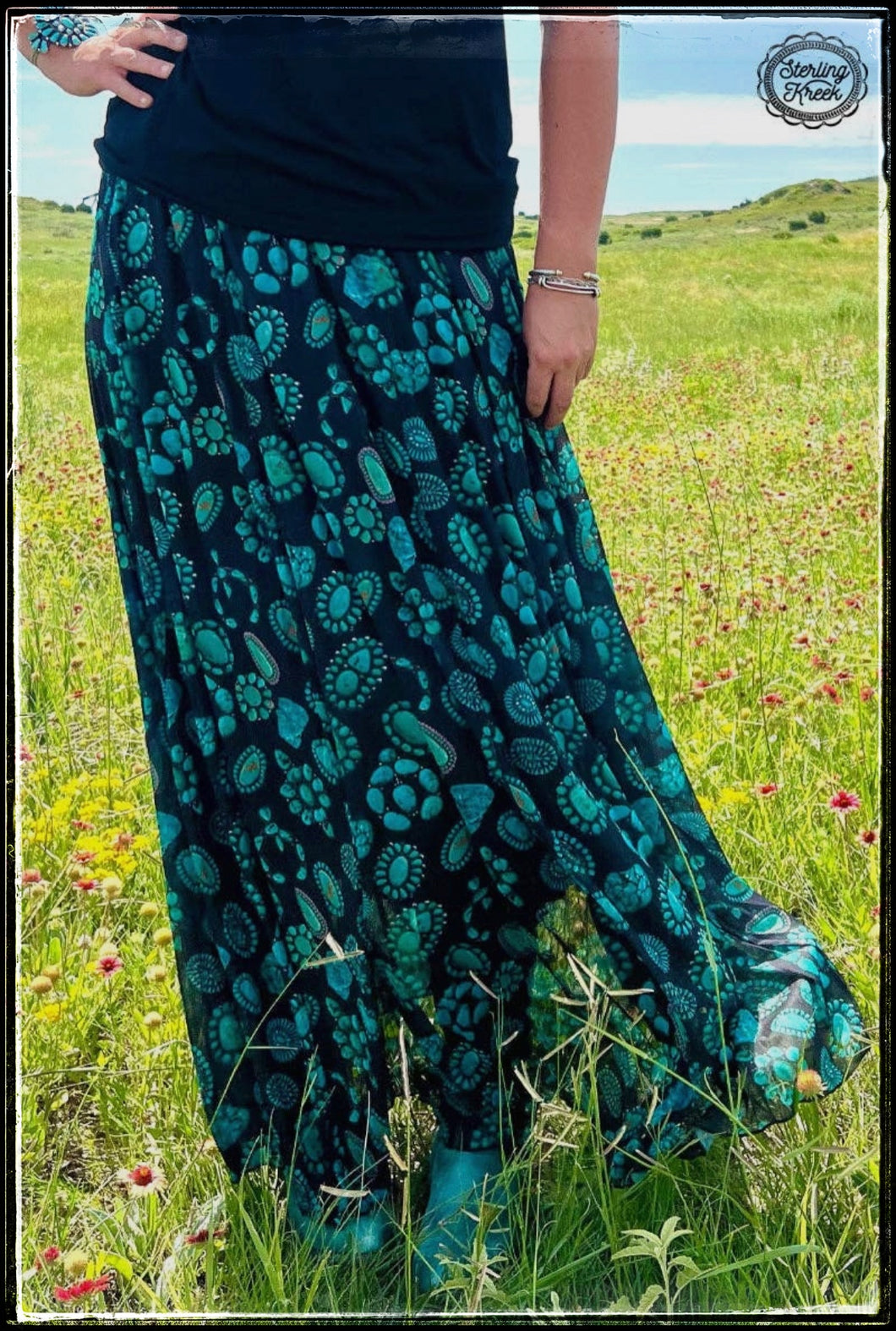 A vibrant turquoise squash blossoms and a black slip underneath maxi skirt